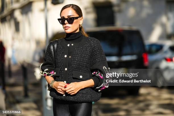 Evangelie Smyrniotaki wears black sunglasses, gold earrings, a black turtleneck pullover, a black checkered tweed with neon pink and white pearls...