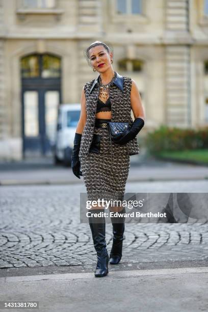 Olga Ferrara wears a black mesh headband, gold earrings, a black and white tweed sleeveless / leather collar jacket from Chanel, a matching black and...