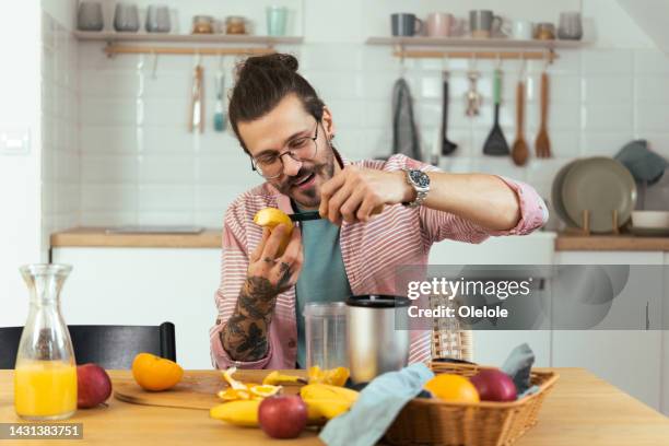 porträt eines jungen mannes, der obst hackt und in einen mixer steckt - mixer stock-fotos und bilder