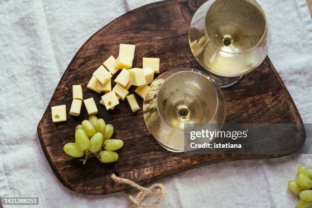 two glasses of white wine, cheese and grapes on wooden board - white wine stockfoto's en -beelden