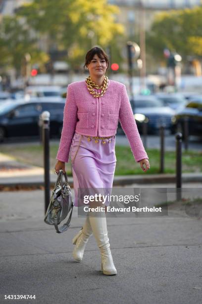 Clervie Rose wears white pearl earrings from Chanel, gold large chain necklace, a pink tweed cropped jacket, a pale purple satin / silk knees skirt,...