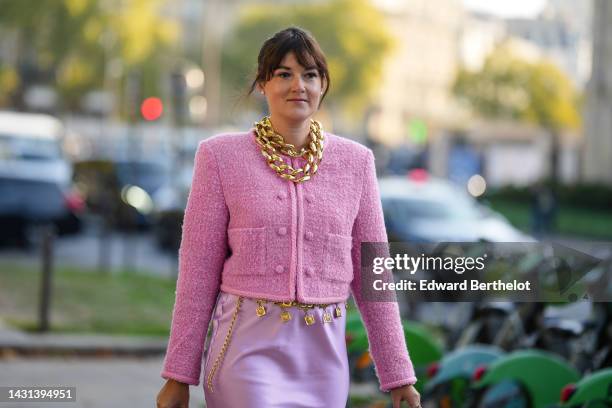 Clervie Rose wears white pearl earrings from Chanel, gold large chain necklace, a pink tweed cropped jacket, a pale purple satin / silk knees skirt,...