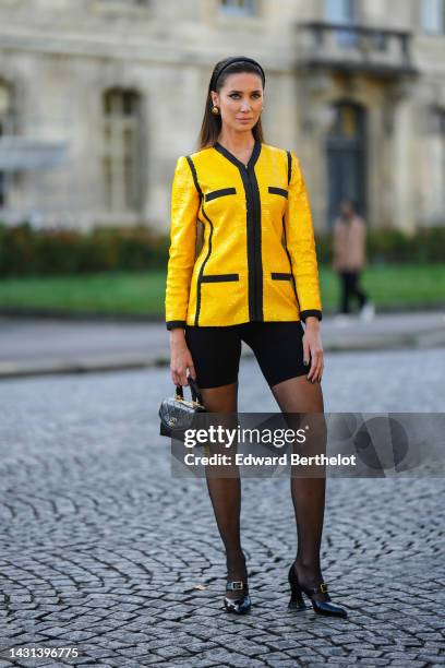 Sabina Jakubowicz wears a black satin headband, black and gold earrings from Chanel, a yellow sequined with black borders jacket, black cyclist...