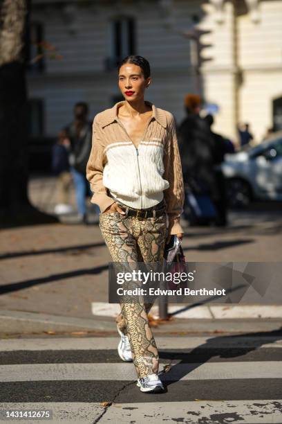 Guest wears a beige and white bicolored braided wool zipper pullover from Miu Miu, diamond earrings, brown shiny leather belts, brown and black snake...