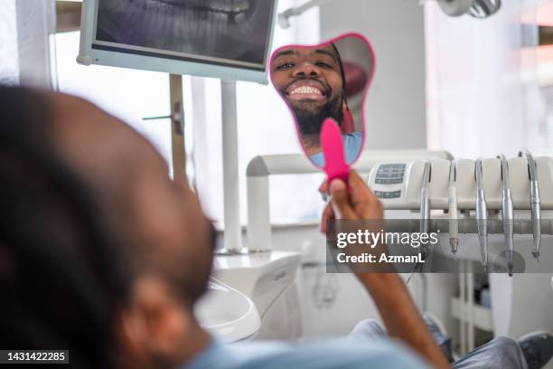 african-american man looking at mirror with smile in dentist’s office - dentists chair stockfoto's en -beelden