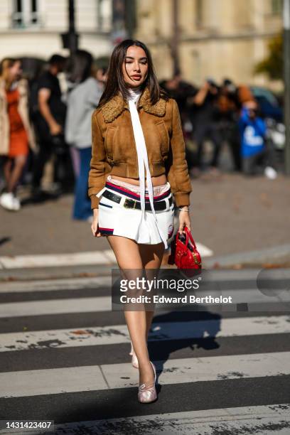 Guest wears black sunglasses, gold earrings, a brown suede with sheep collar bomber coat from Miu Miu, a white tulle turtleneck t-shirt, a white...