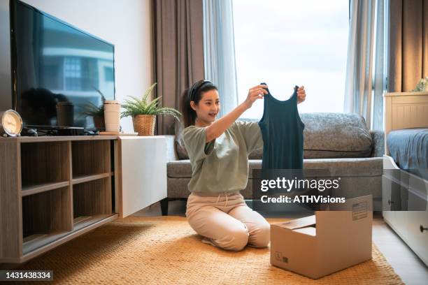 woman opening a shipment delivery and looking at the clothing purchased at home. - online shopping opening package stockfoto's en -beelden