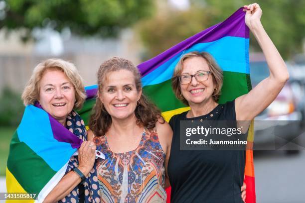 lächelnd glücklich reife und ältere lesbische frauen, die mit einer regenbogenfahne posieren - lesbe stock-fotos und bilder