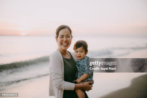 happy mother holding baby on beach at sunset - japanese mom stock-fotos und bilder