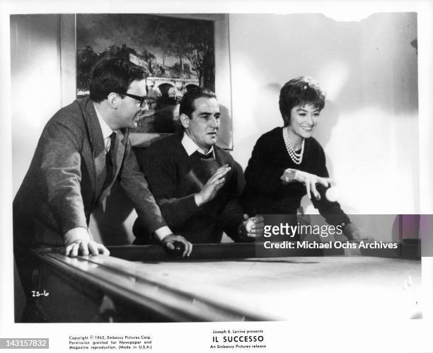Vittorio Gassman, Jean Louis Trintignant and Anouk Aimee standing at a pool table together in a scene from the film 'Il Successo', 1965.