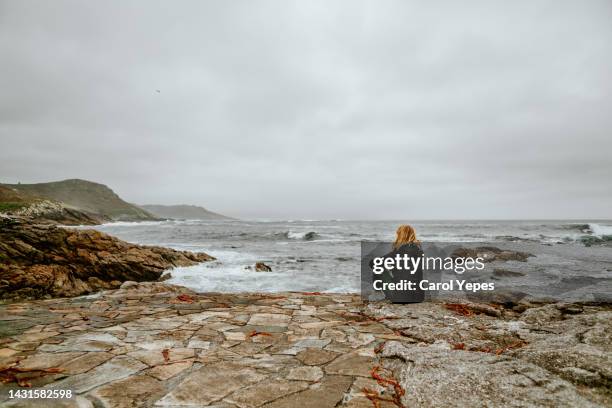 one woman standing on the rock looking out the waves and the sea - corunna stock pictures, royalty-free photos & images