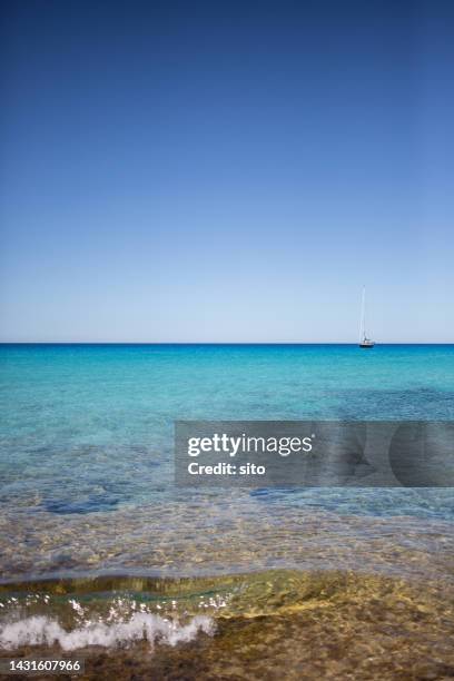 turquoise waters and a single sailboat at the horizon - islas baleares fotografías e imágenes de stock