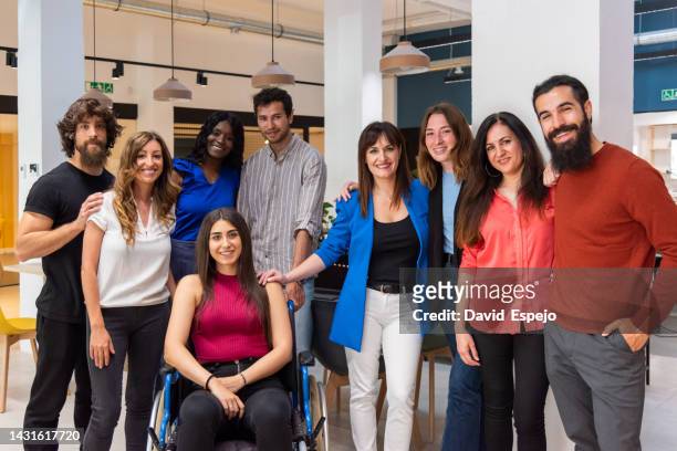 diverse group of work colleagues looking at camera and smiling while posing together in a coworking space. - gruppo dei 20 stock-fotos und bilder