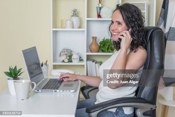 cheerful female freelancer talking on smartphone and using laptop at home - laptop netbook fotografías e imágenes de stock