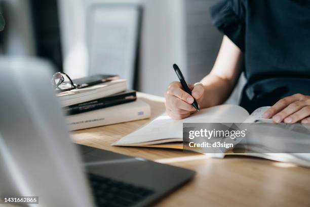 cropped shot of focused young asian woman reading book and making notes at home, concentrates on her studies. further education, continuous learning concept - law stock-fotos und bilder