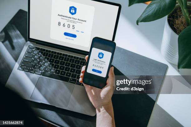 cropped hand of woman using mobile device with two-factor authentication (2fa) security while logging in securely to her laptop. privacy protection, internet and mobile security - autenticación digital fotografías e imágenes de stock