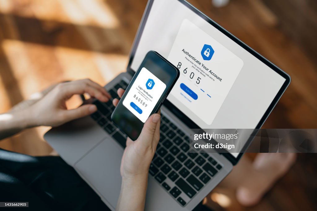 Cropped hand of woman using mobile device with Two-Factor Authentication (2FA) security while logging in securely to her laptop. Privacy protection, internet and mobile security