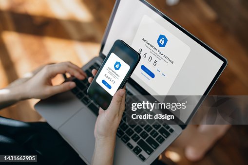 Cropped hand of woman using mobile device with Two-Factor Authentication (2FA) security while logging in securely to her laptop. Privacy protection, internet and mobile security Cropped hand of woman using mobile device with Two-Factor Authentication (2FA) security while logging in securely to her laptop. Privacy protection, internet and mobile security