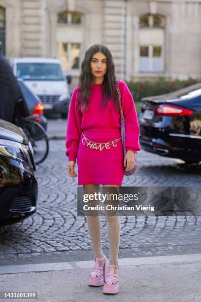 Guest wears belt with logo print, pink skirt, cashmere jumper, pink bag outside Chanel during Paris Fashion Week - Womenswear Spring/Summer 2023 :...