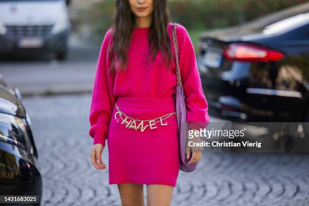 Guest wears belt with logo print, pink skirt, cashmere jumper, pink bag outside Chanel during Paris Fashion Week - Womenswear Spring/Summer 2023 :...