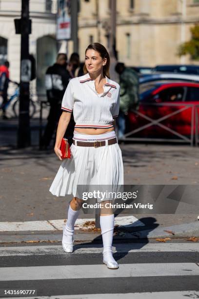 Camille Charriere wears white cropped polo shirt, pleated skirt with brown belt, white knee high socks, red bag outside Miu Miu during Paris Fashion...