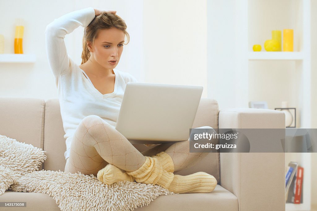 Beautiful, young,  thoughtful, blond woman using laptop at home