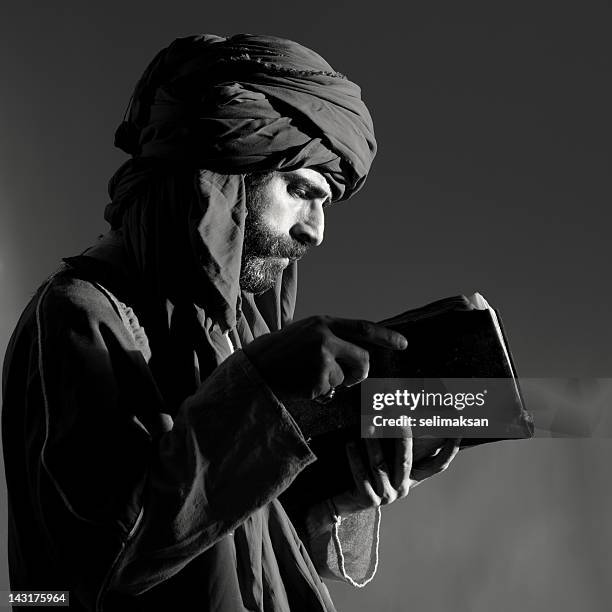 bearded man with headscarf reading old antique book - tulband stockfoto's en -beelden