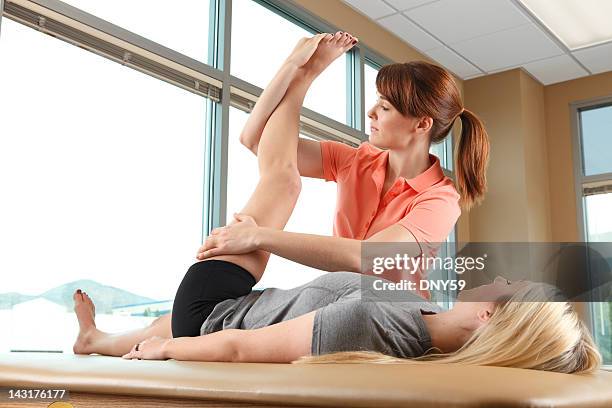 physical therapist helping a woman stretch her leg - massage table stock pictures, royalty-free photos & images