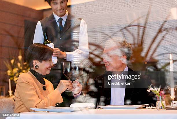 mature japanese couple dining at a restaurant seen through window. - asian couple dining stockfoto's en -beelden