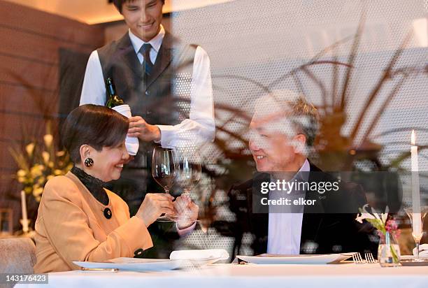 mature japanese couple dining at a restaurant seen through window. - japanese restaurant stock pictures, royalty-free photos & images