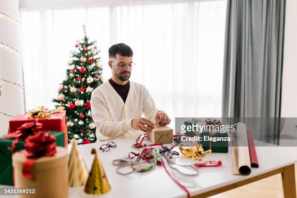 young man wrapping christmas gifts - small business saturday stock pictures, royalty-free photos & images