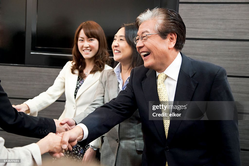Smiling Japanese businessmen and businesswomen shaking hands.