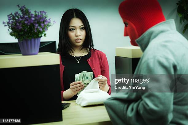 criminal robber robbing an asian retail bank teller at counter - bankrover stockfoto's en -beelden