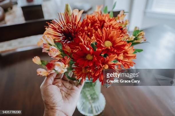woman arranges flowers in vase on dining table - centerpiece stock-fotos und bilder