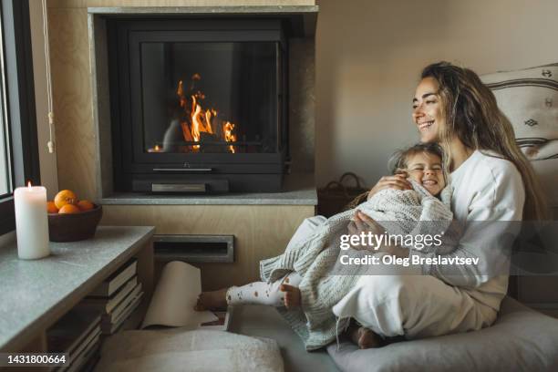 mother and cute little daughter laughing and having fun together at home near fireplace - fireplace cosy stock pictures, royalty-free photos & images