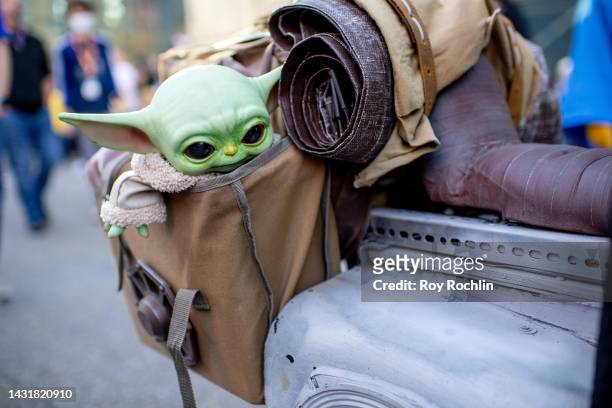 Cosplayer dressed as the Mandalorian poses with a Grogu doll hanging in his bag during New York Comic Con 2022 on October 08, 2022 in New York City.