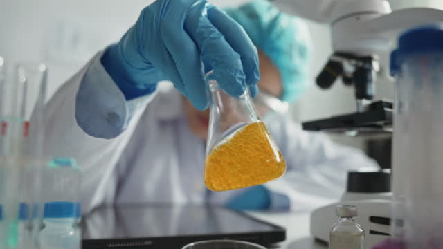 장갑을 끼고 있는 과학자의 손은 노란색 액체가 묻은 멸균 플라스크를 잡고 있다. 석유 연구 및 독성 액체 개념