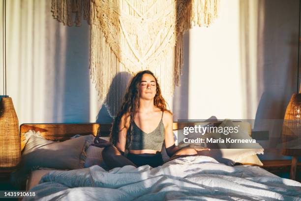 young woman meditating on bed at home. - morning exercise stock pictures, royalty-free photos & images