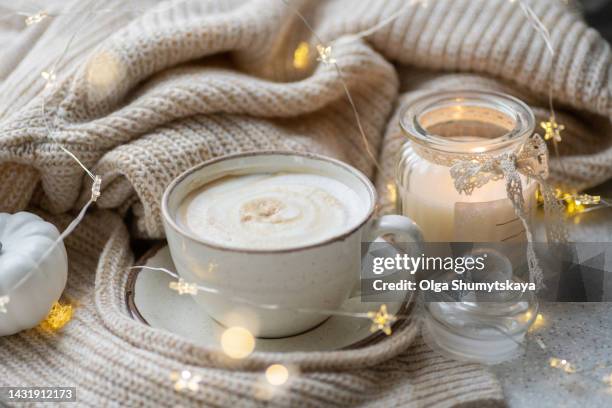 a large cup of coffee with milk on the background of a warm sweater and lights. - amplified heat stock pictures, royalty-free photos & images