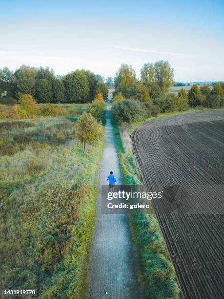 drone view on man running on track among fields in fall - germany training stock pictures, royalty-free photos & images