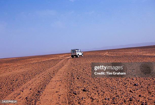 White Land Rover crossing the stony desert floor leaving a dust trail behind in the Sahara Desert, Morocco