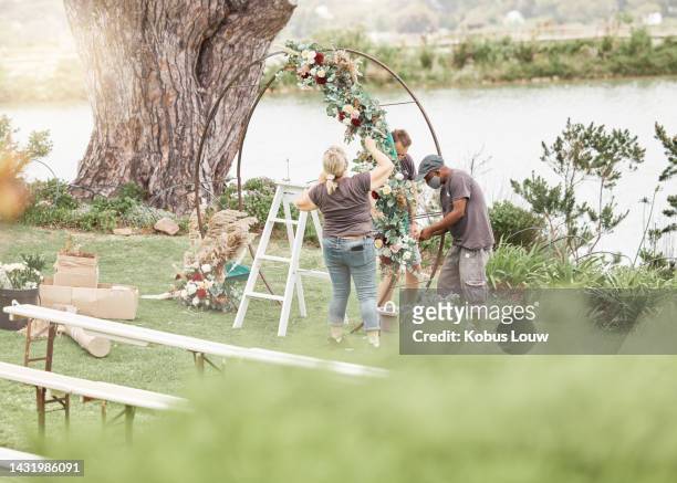 wedding ceremony, florist or event planner decorating arch with flowers for floral theme by quiet, calm and beautiful lake with team. decoration, marriage and romance with decor staff for celebration - event planner stock pictures, royalty-free photos & images