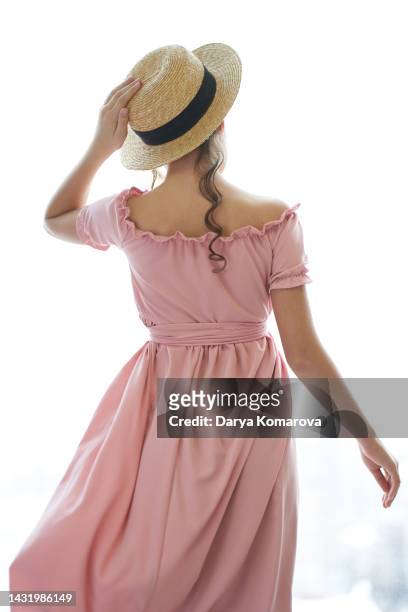 a girl in a pink dress and a straw hat is standing from behind and looking into the distance on a white background. retro style, vintage, design element for product. book cover design with copy space, historical period costume of 19th, 20th century. - girl white dress stock pictures, royalty-free photos & images