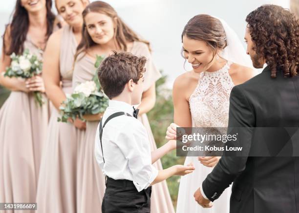 boy giving ring to smile couple at wedding with excited bridesmaids looking. wedding couple at ceremony in gown and suit receive jewelry from child for marriage, relationship and commitment. - small wedding ceremony stock pictures, royalty-free photos & images