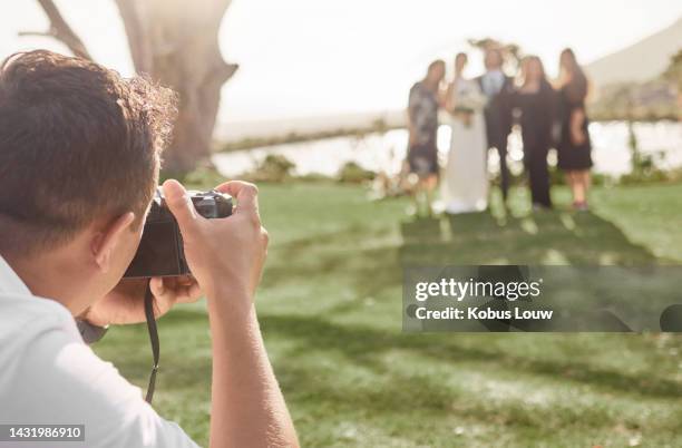 wedding, photography and photographer with bride and groom posing for a picture with wedding guests outdoors. photo, camera and friends and family celebrating with just married couple at park - photographer stock pictures, royalty-free photos & images