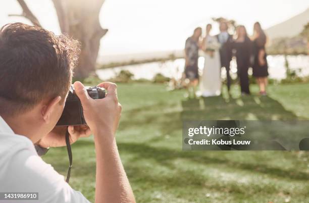 wedding, photography and photographer with bride and groom posing for a picture with wedding guests outdoors. photo, camera and friends and family celebrating with just married couple at park - wedding photographer stock pictures, royalty-free photos & images