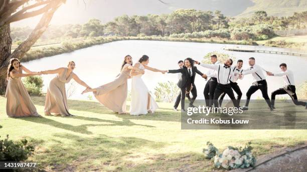 wedding comedy, bride and groom party pulling, being funny and silly trying to separate married couple by a lake in nature. happy men and women together for a marriage celebration together outside - white dress stock pictures, royalty-free photos & images