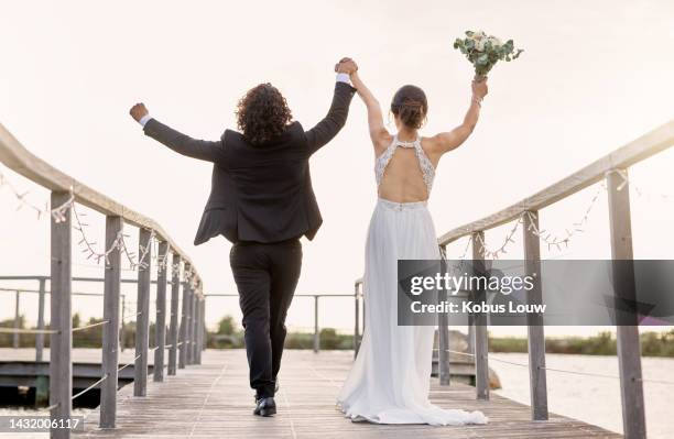 paar, spaziergang und hochzeit, feier der liebe mit händen im himmel und brücke am see oder damm zusammen. mann, braut mit blumenstrauß und spaziergang am fluss, glücklich am tag der hochzeit im sommer - frisch verheiratet stock-fotos und bilder