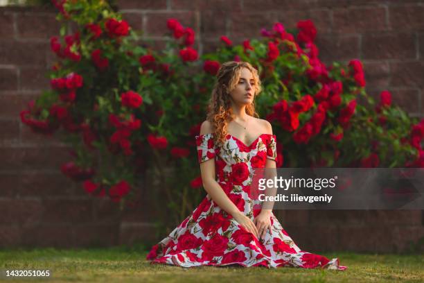 curly redhead model on summer nature background. spring rose flower garden. fabulous woman in dress. awesome flowers wall. blonde lady. portrait. trendy look. modern art. sunset light. roses bush - ginger bush stock pictures, royalty-free photos & images