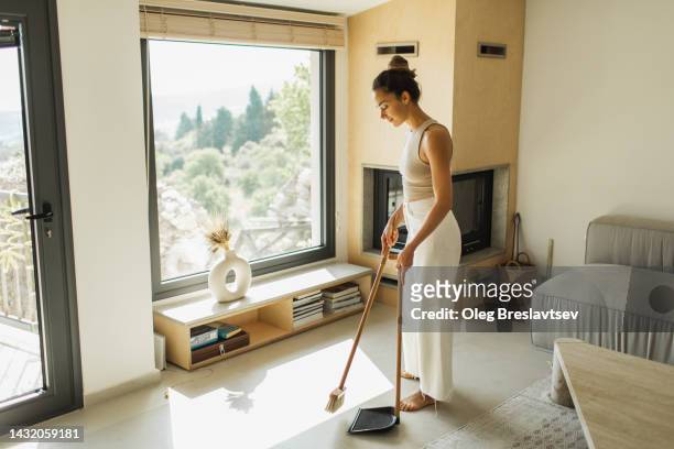 young woman sweeping the floor and cleaning house. household chores - escoba fotografías e imágenes de stock